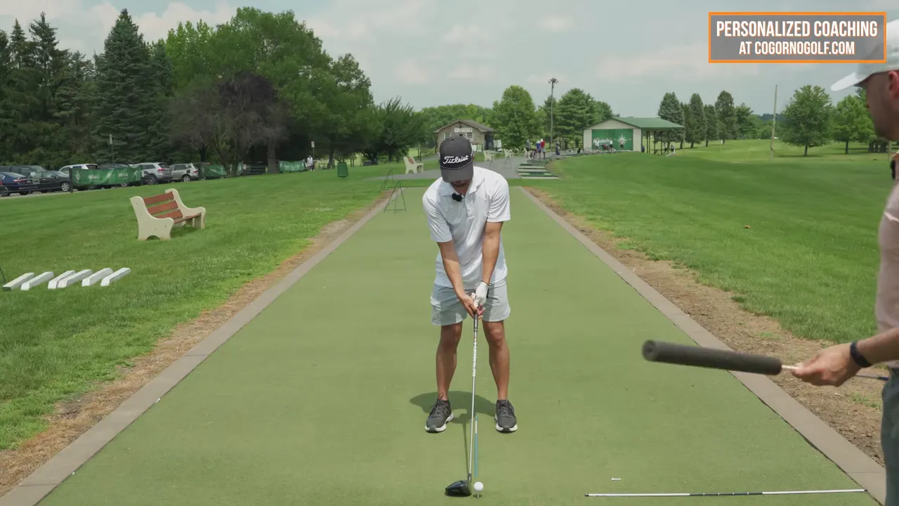 Golfer at address with driver on a tee, alignment rods showing ball and club relationship from a front-on view
