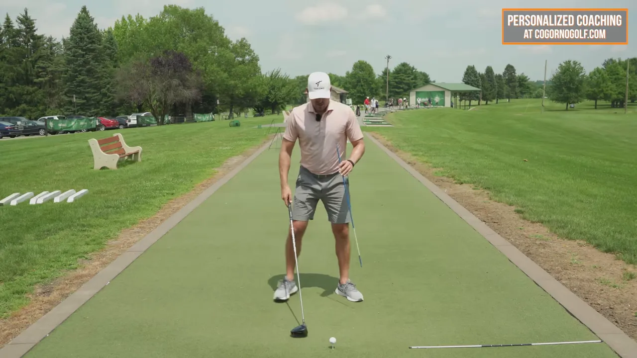 golfer setting up to hit a driver with an alignment rod near his lead armpit and the ball on a tee