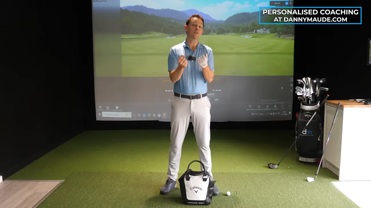 Golf coach with a training bag placed at his feet in an indoor simulator ready to demonstrate the bag-sling drill