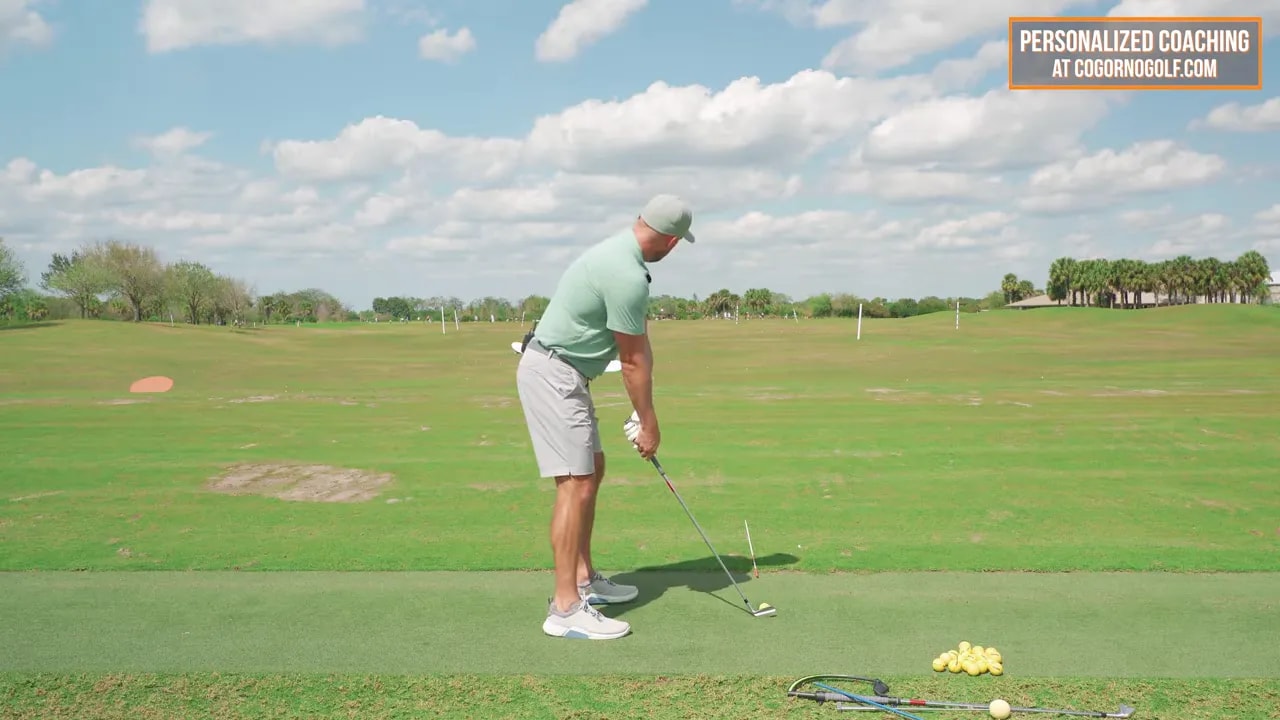 Calm, clear address view of an instructor with a golf ball, practice balls and training aids on the mat ready for drills