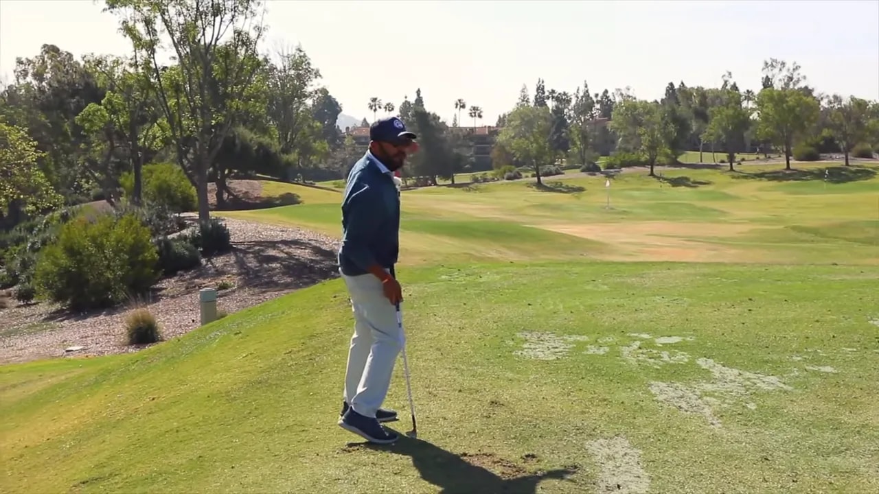Golfer standing over a wedge shot aligned to the intended swing path with the green and flags visible ahead