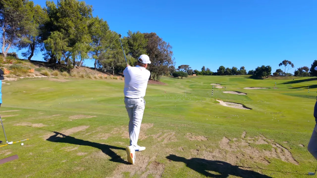 Golfer in follow-through on a practice range showing a balanced finish and the fairway ahead