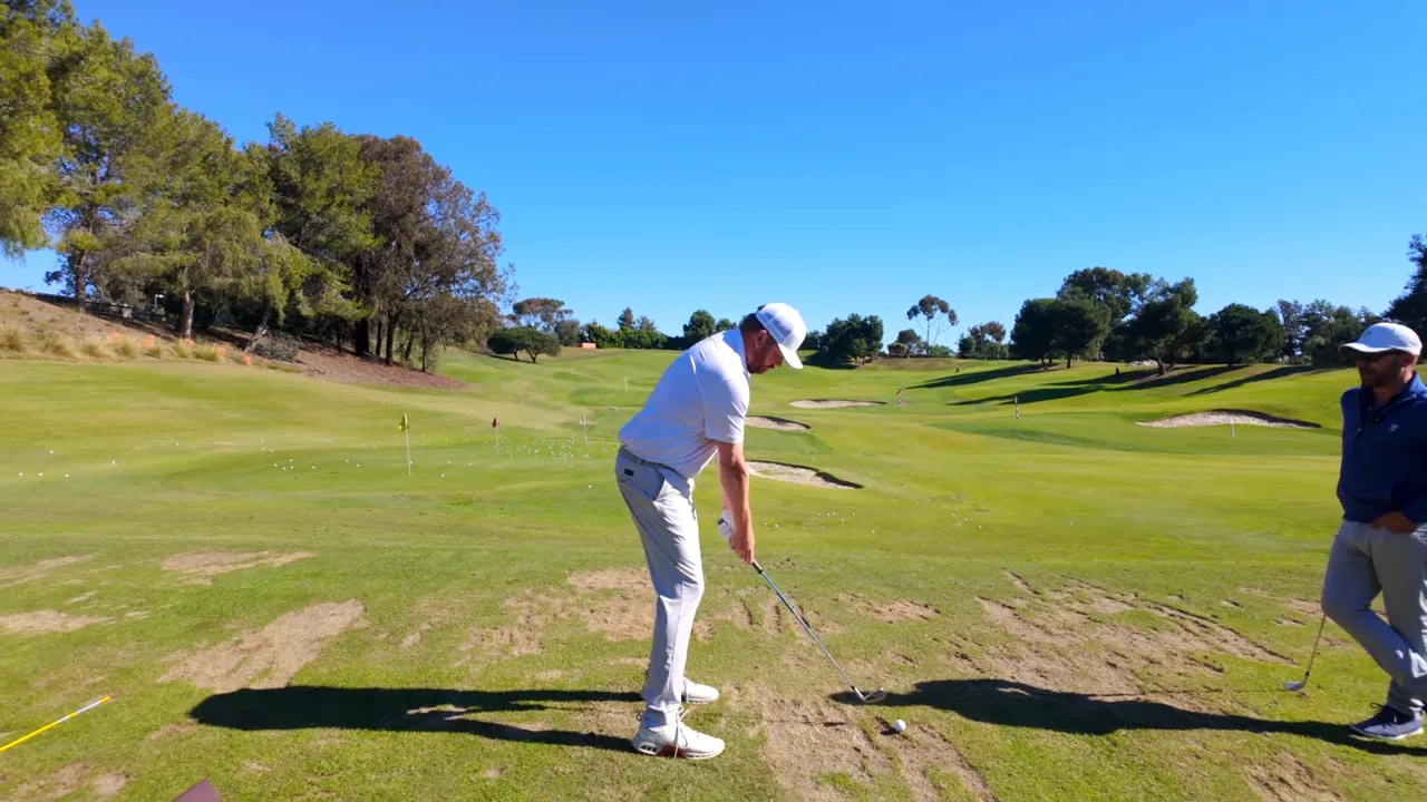 Golfer at address demonstrating left-hand grip and club position with coach observing