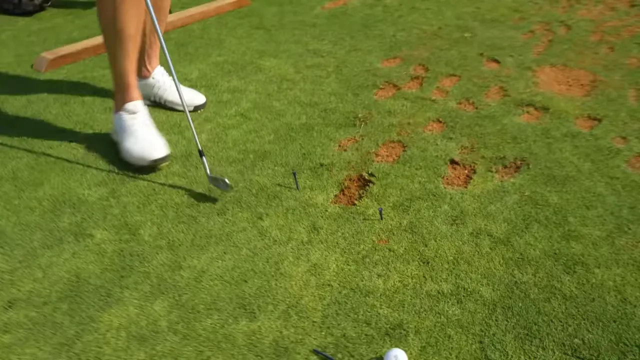 Golf ball on turf with divot marks and tee markers showing the low point shifted toward the target