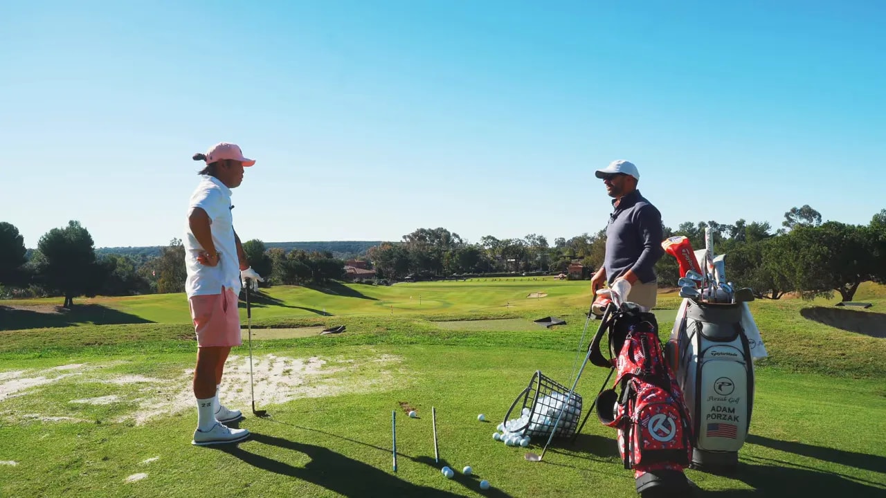 Two golfers discussing strategy on the driving range with clubs and bags visible