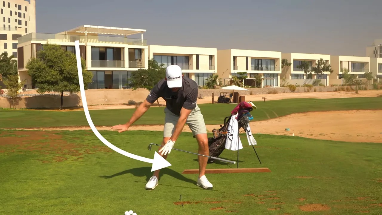 Face‑on delivery frame showing hands lowering toward the ball and an overlaid arrow illustrating the club's down‑then‑through path