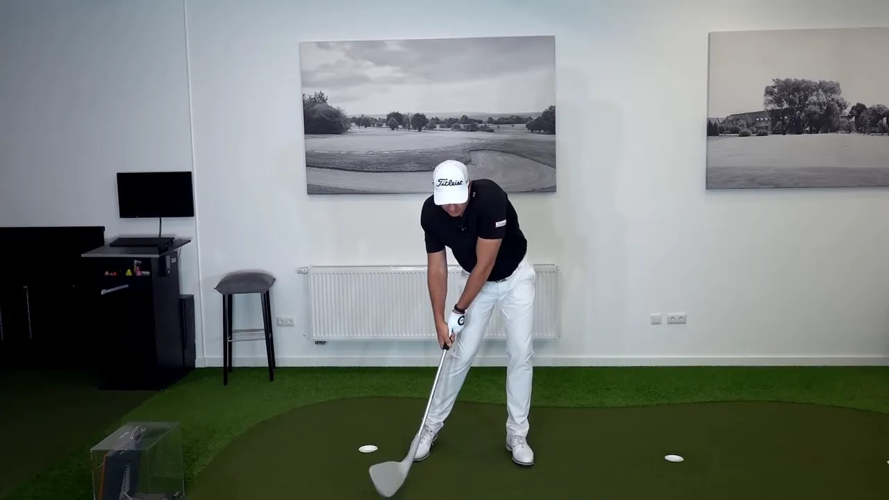 Golfer demonstrating impact position with hands ahead of the ball and forward shaft lean over the turf.
