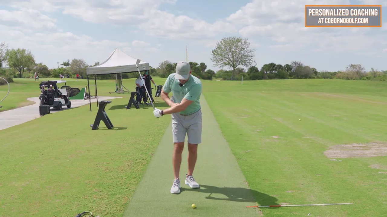 Frontal view of the instructor rotating through impact with the lead arm and club visible to demonstrate glove alignment and rotation.