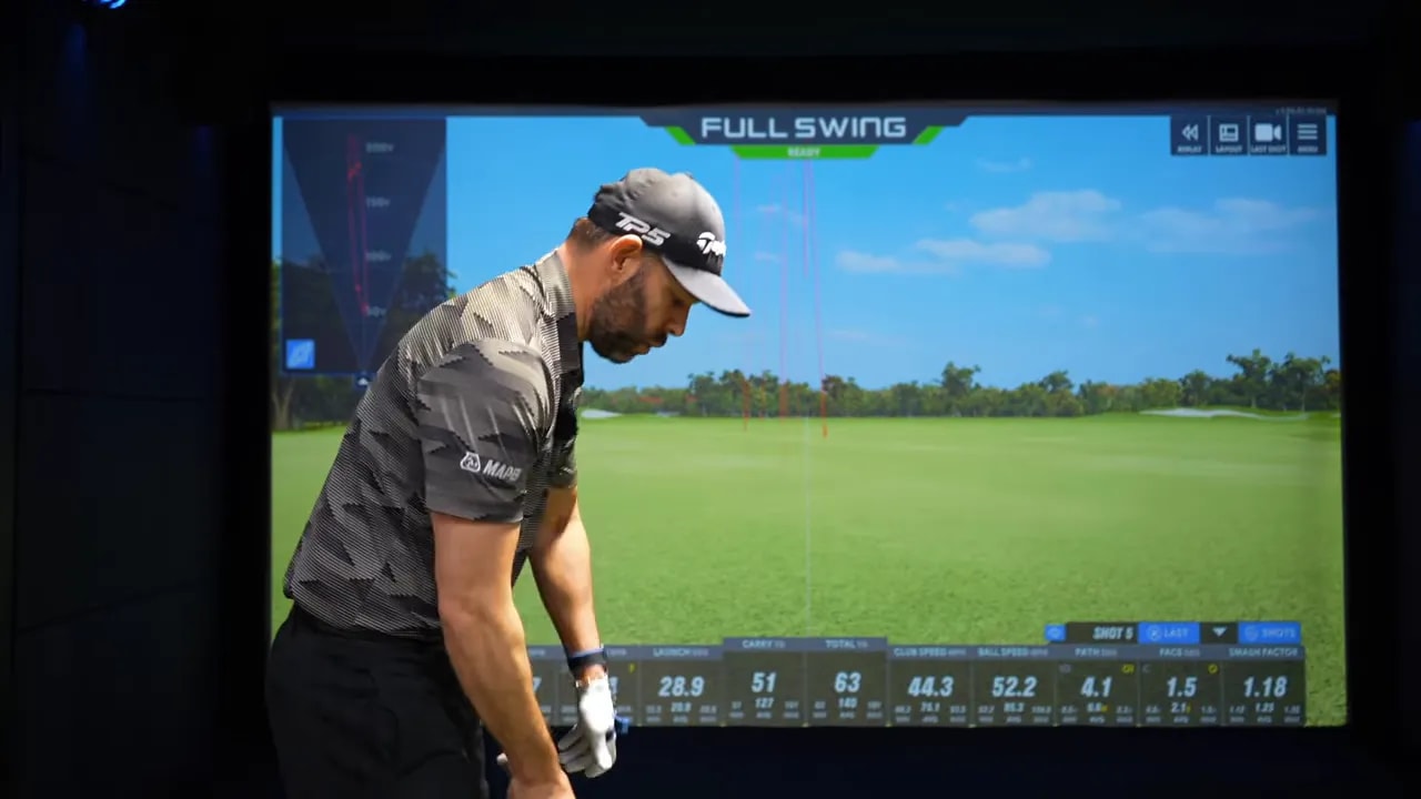 Side view of golfer at address in indoor simulator showing lead hand on the grip and wrist set