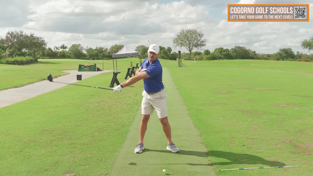 Golfer in follow-through with left shoulder up-and-back and extended arms after a driver swing