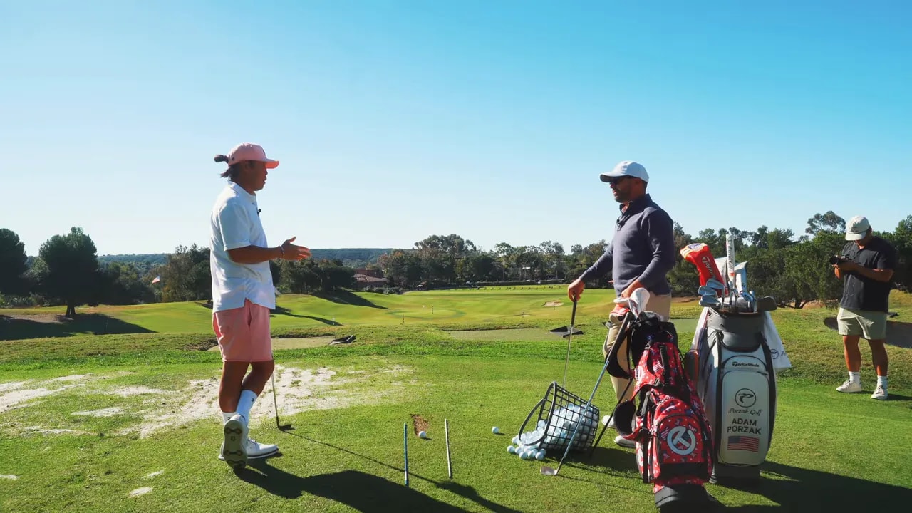Two golfers discussing strategy on a practice tee with golf bags and a basket of practice balls