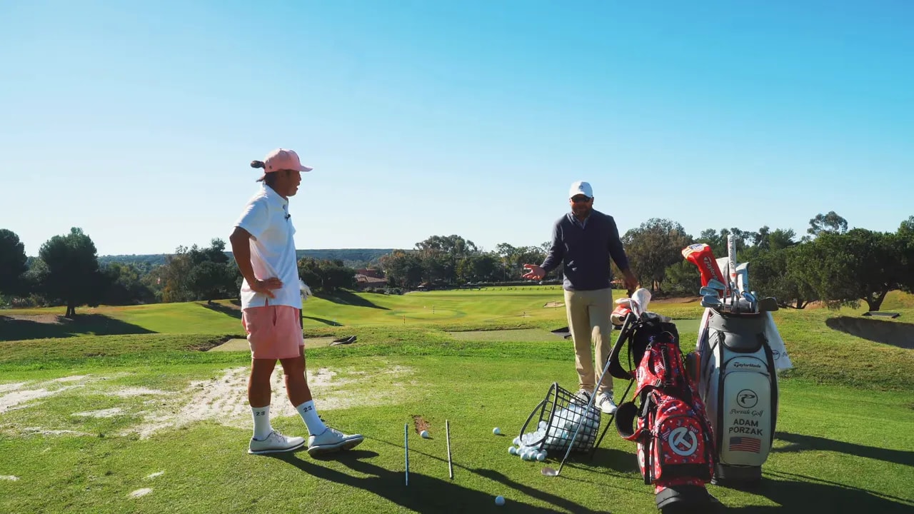 Two golfers on a practice tee reading the course and discussing strategy with golf bags and a wide fairway behind them