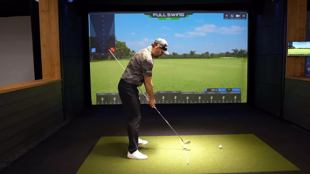 Wide view of golfer at address with a long alignment stick held along the club tracing toward the ground-stick