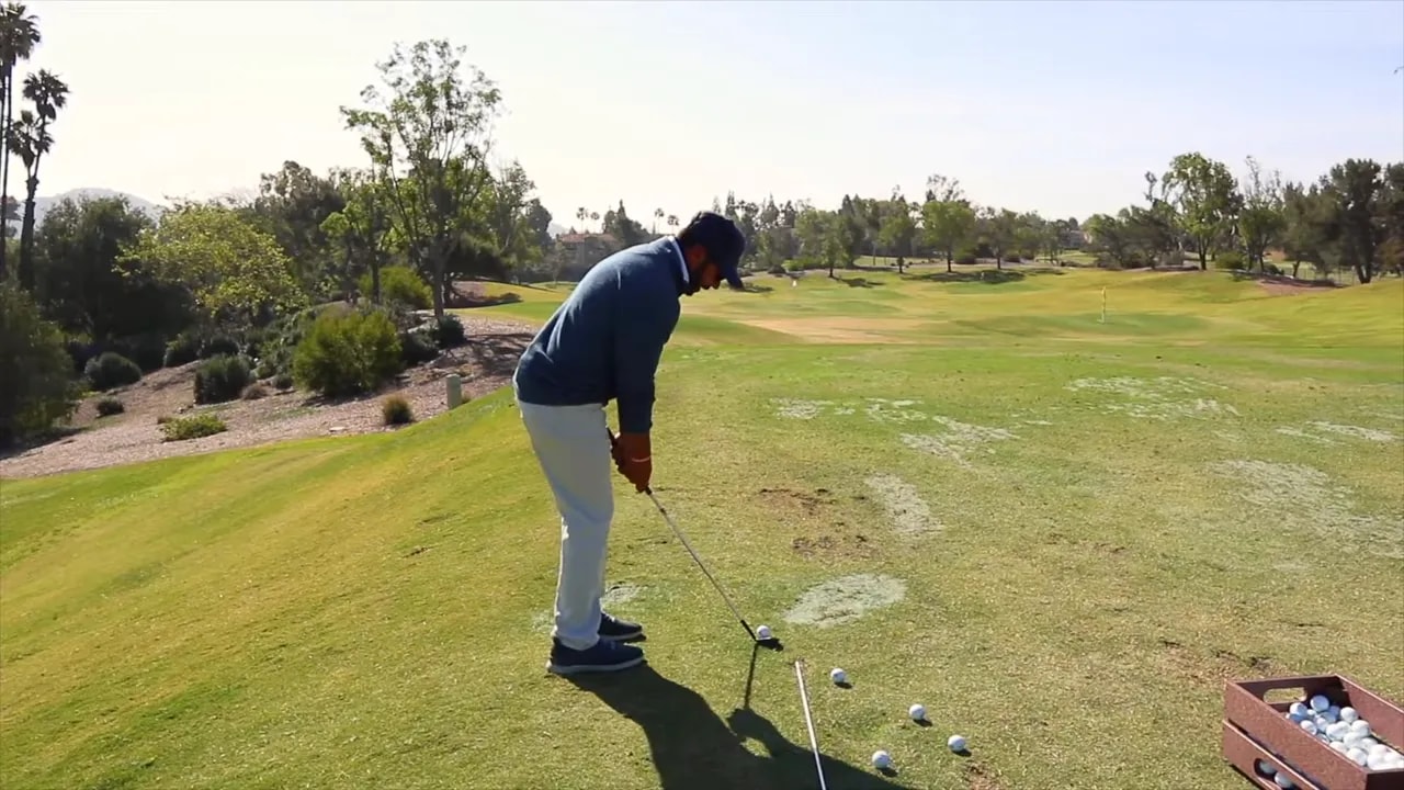 Golfer at address with a wedge, alignment rod on the ground and practice balls demonstrating ball position.