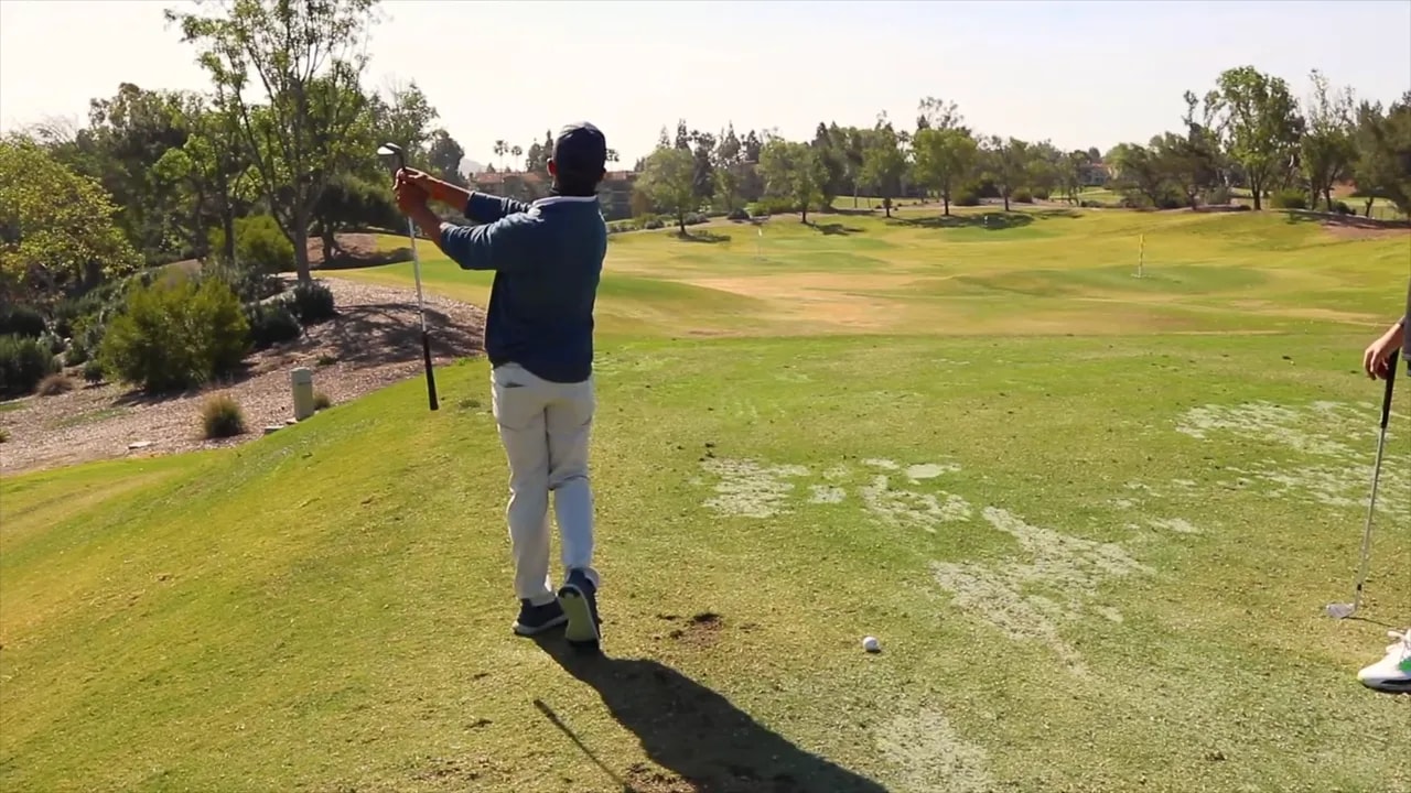 Golfer in follow-through after a wedge shot showing forward weight shift and club across chest