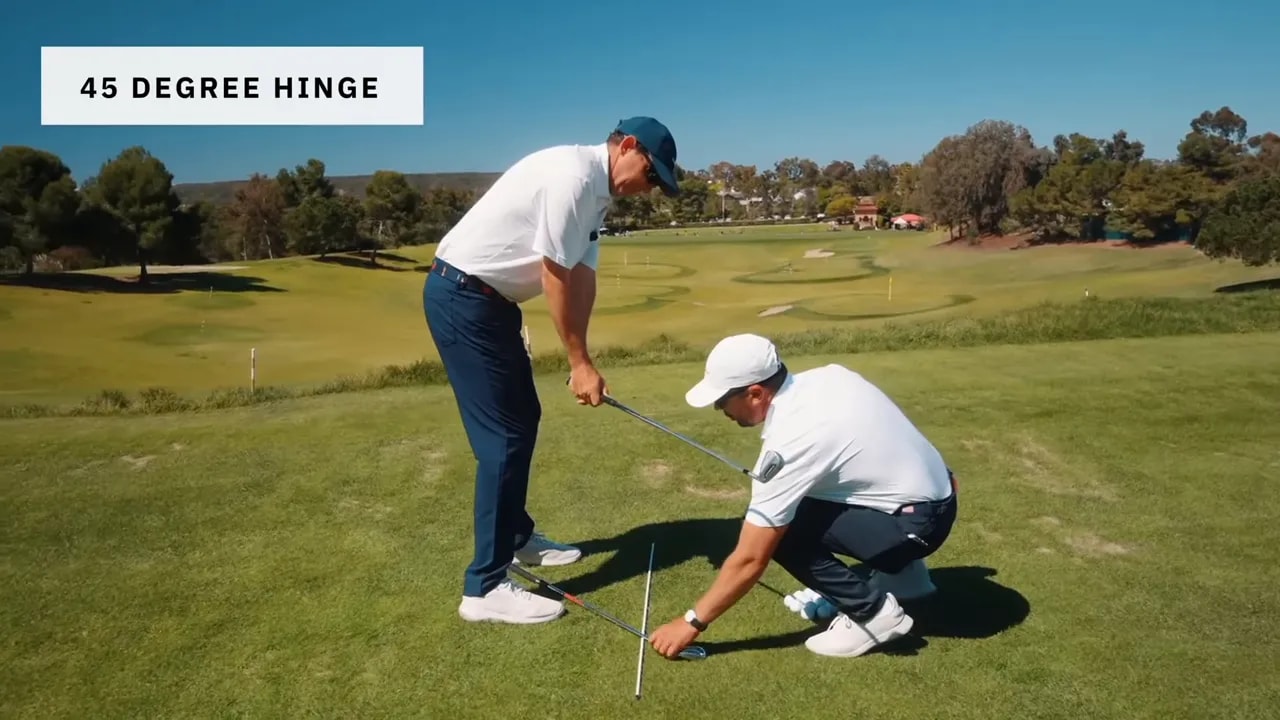 Instructor showing a 45 degree hinge with alignment rods while adjusting the golfer's club position.