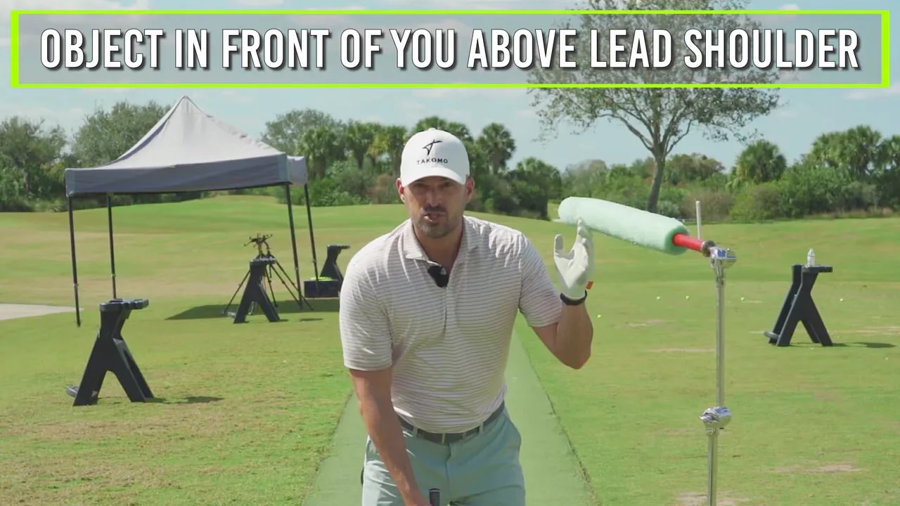 Coach demonstrating the advanced drill with a foam object positioned at lead shoulder height to train keeping the head back while the hips drive forward.