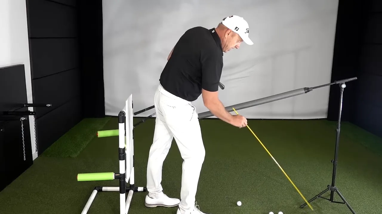 Golf instructor demonstrating an alignment stick placed beside the hands to train returning to the original shaft plane.