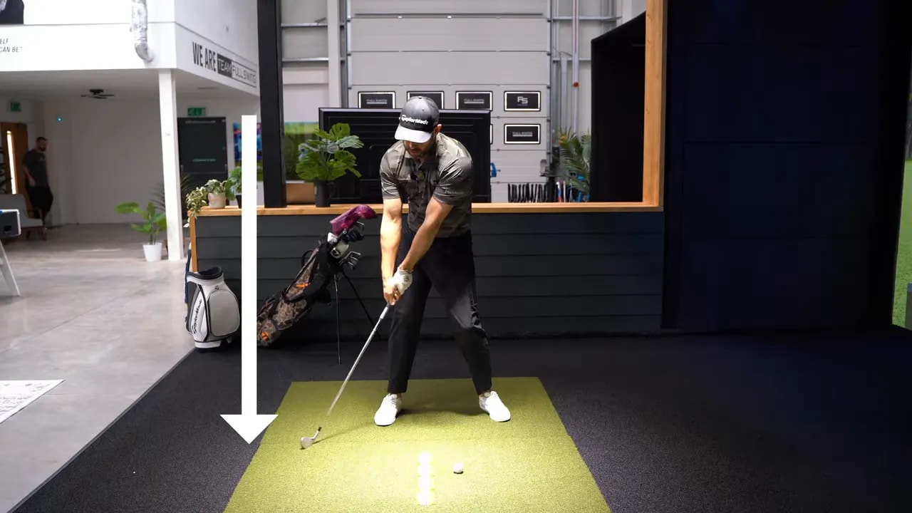 Golfer mid-downswing with a large downward arrow showing the clubhead path toward the turf and mat