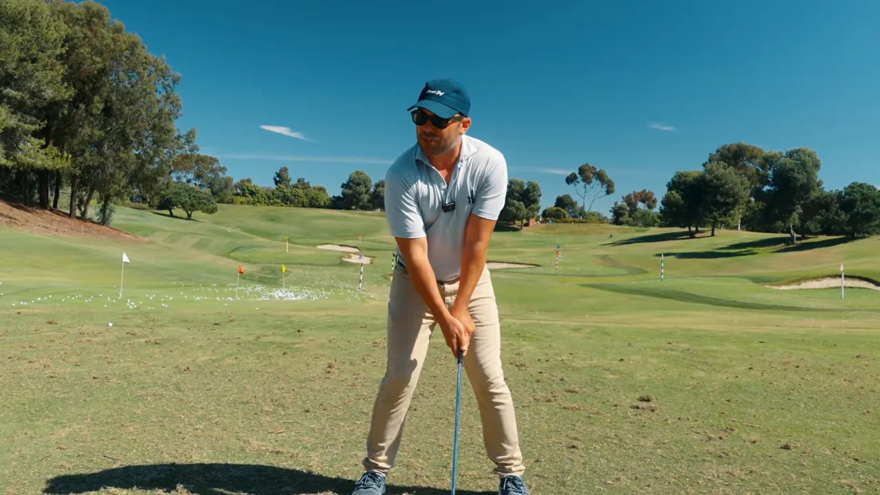 Golfer instructor positioning at address to demonstrate the ball-behind chest drill for contact and direction
