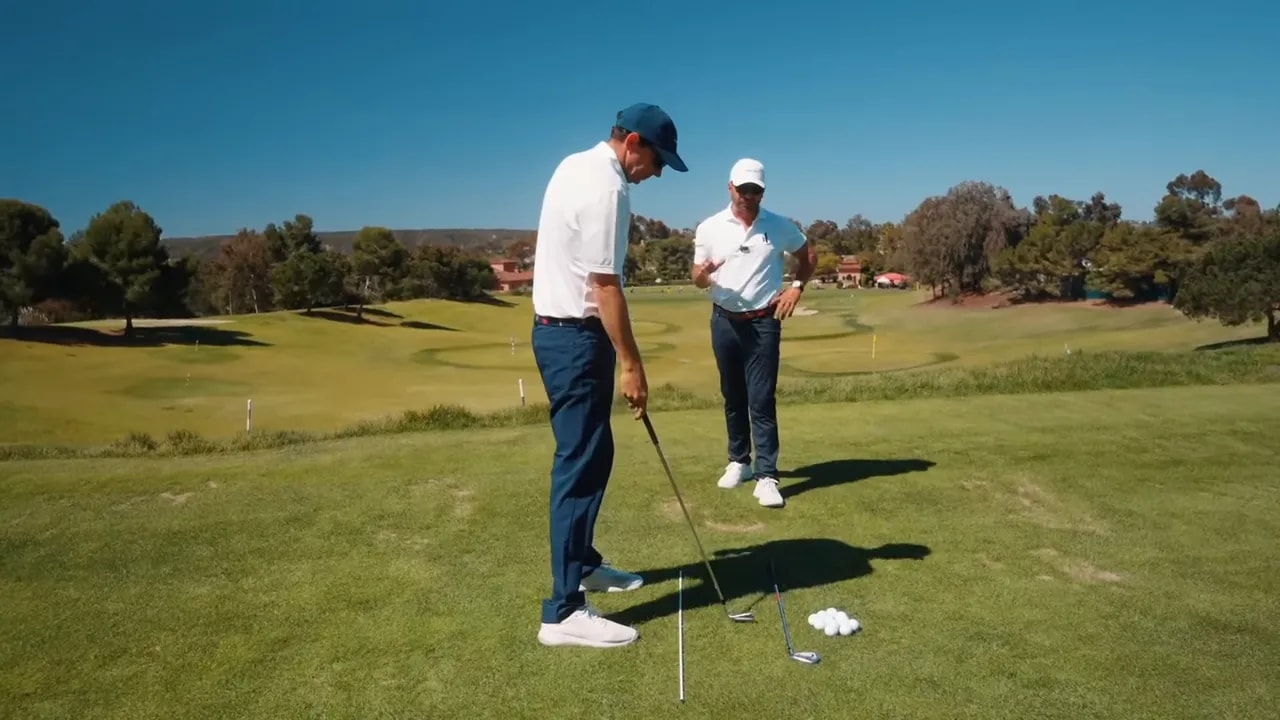 Golfer at address with the club butt pointing toward the ball while the coach watches, illustrating the 'love zone' setup check.