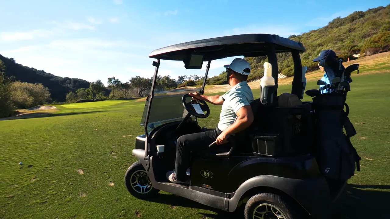 Golf cart near the tee with a clear view down the fairway and a bunker, player preparing for the shot
