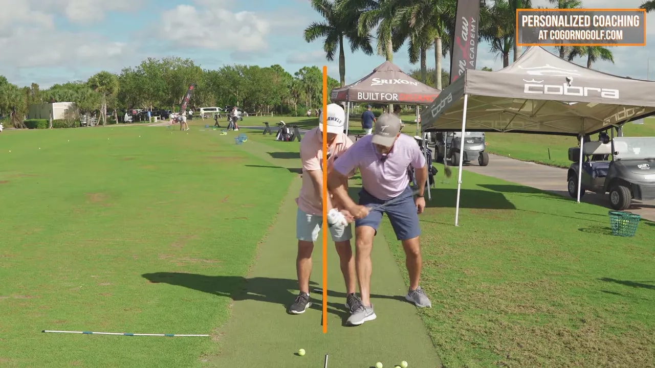 Golfer demonstrating committed forward lean for turf-first punch-down contact with coach nearby