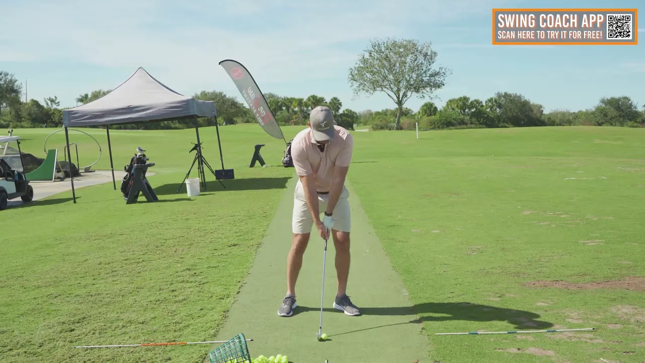 Face-on golf setup at the driving range with club at address and alignment rods on the mat