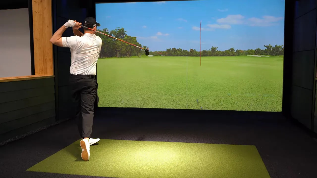 Golfer at address demonstrating driver grip and clubface delivery in a golf simulator