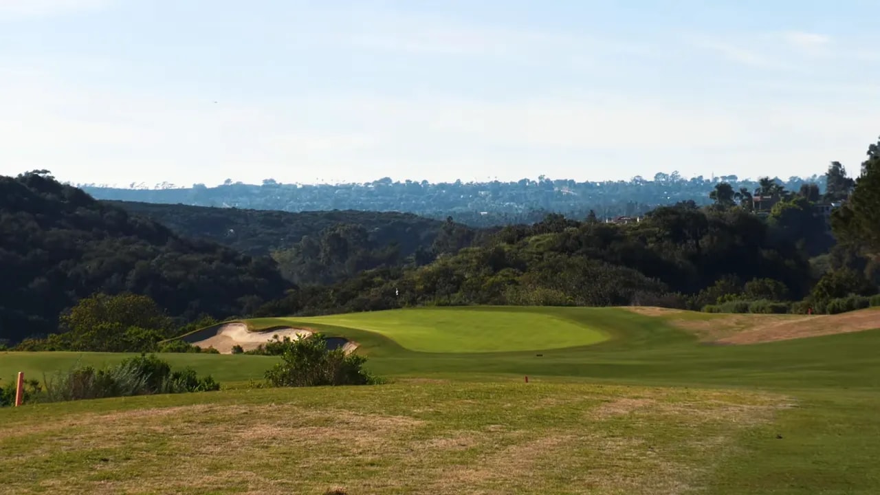 Wide view of a green with a bunker and surrounding fairway and hills