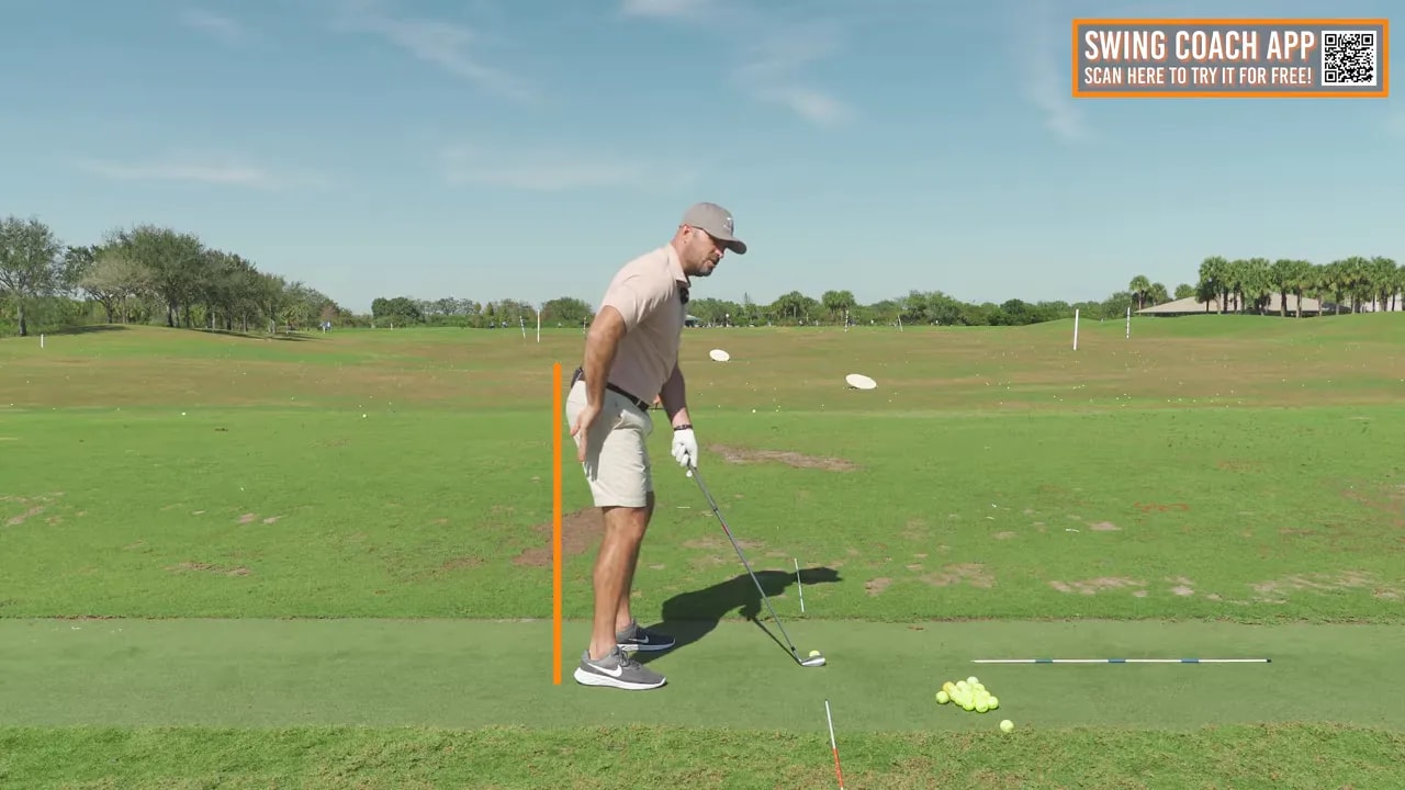 Side-on view of a golfer at address with an orange vertical reference line behind the hips showing hip alignment