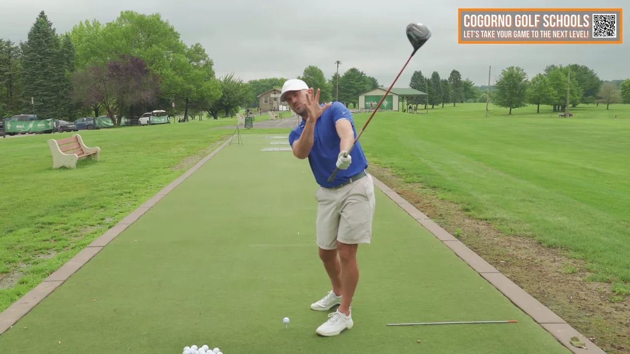 Golf instructor on the range in mid follow-through demonstrating the free release, head held back and trail shoulder down.