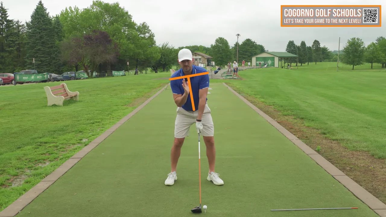 Instructor at address demonstrating lead-side tilt with orange overlay lines highlighting shoulder tilt and chest alignment; ball on tee and driver visible.
