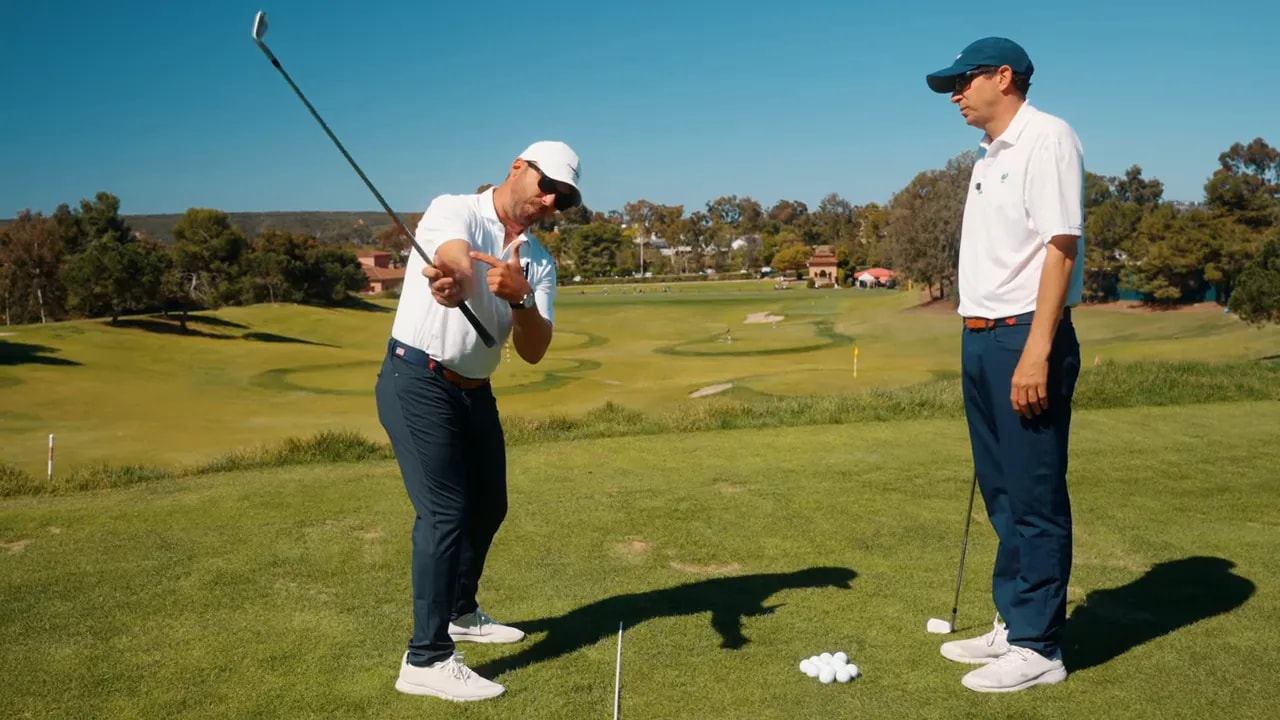 Instructor demonstrating a one-arm takeaway with the club raised and pointing to forearm rotation to show the correct path and reduced trail-hand manipulation.