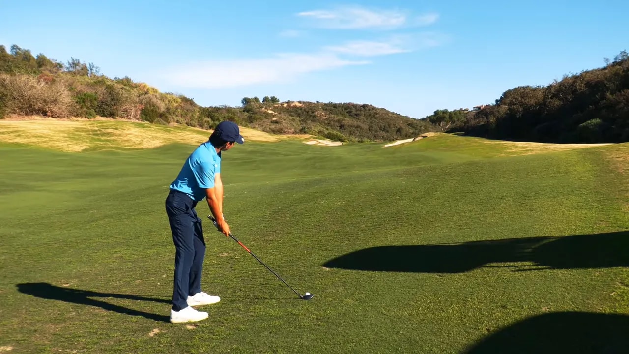 Golfer preparing a fairway shot with bunkers and the long approach visible ahead on a par 5