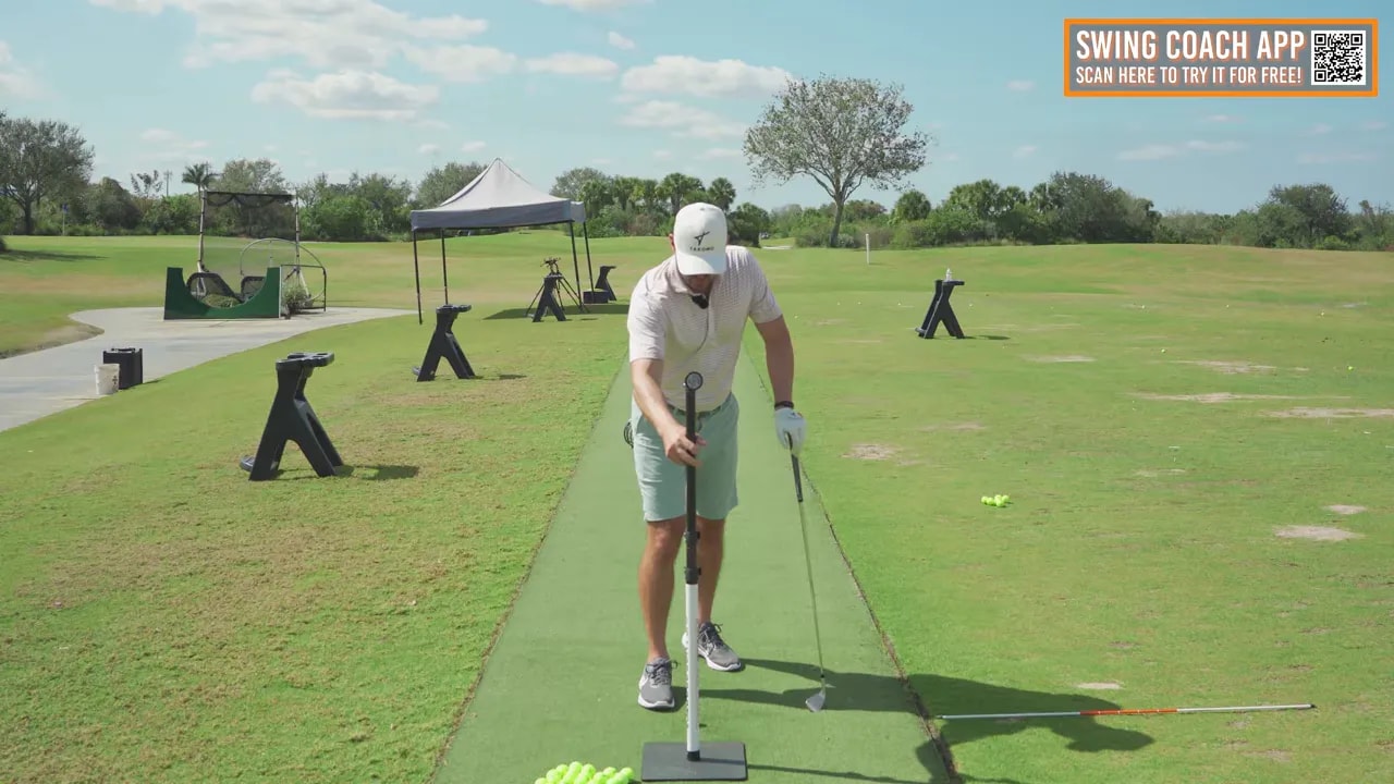 Golf instructor placing a vertical front object on a stand directly in line with the ball on a practice mat to create a chest-height visual for the drill.