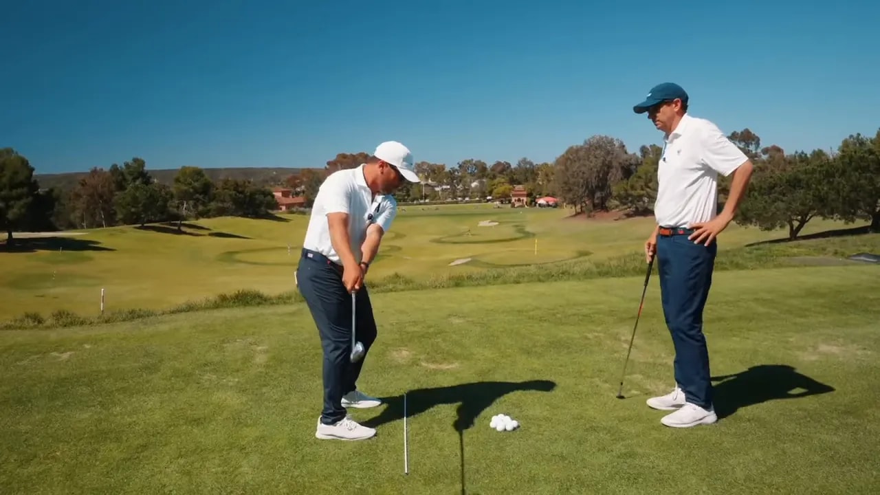 Golfer paused at pocket height with the club beginning to hinge and an alignment rod on the ground