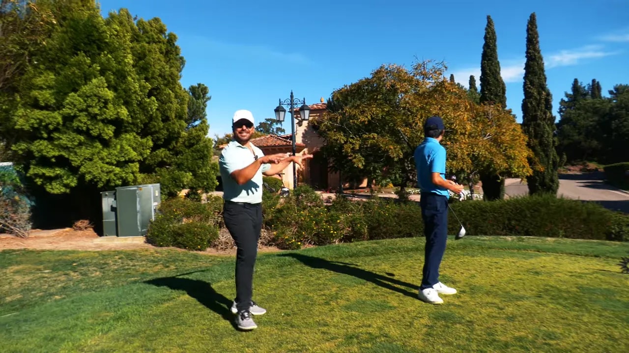 Golf instructor pointing while another player looks toward the fairway from the tee box