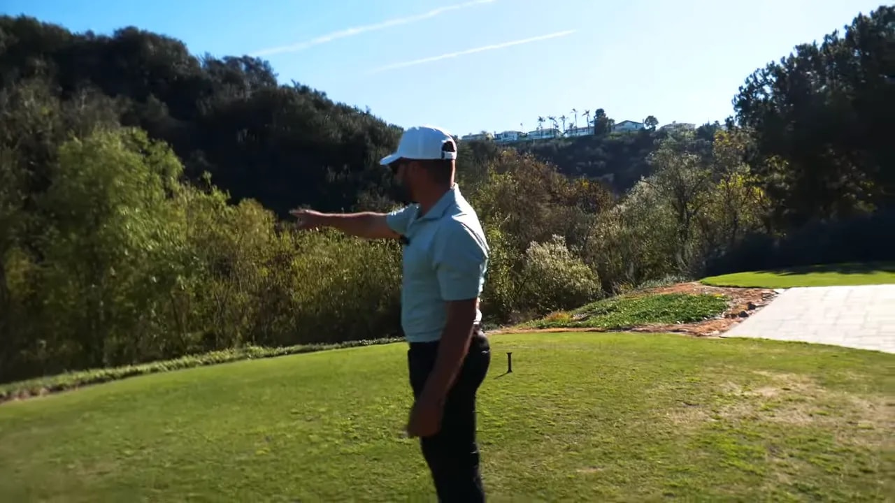 Golfer standing on the tee pointing toward the fairway and indicating a safer target away from the drop