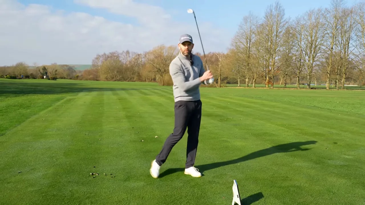 Golf instructor demonstrating a rhythm-based practice move with an iron on the fairway