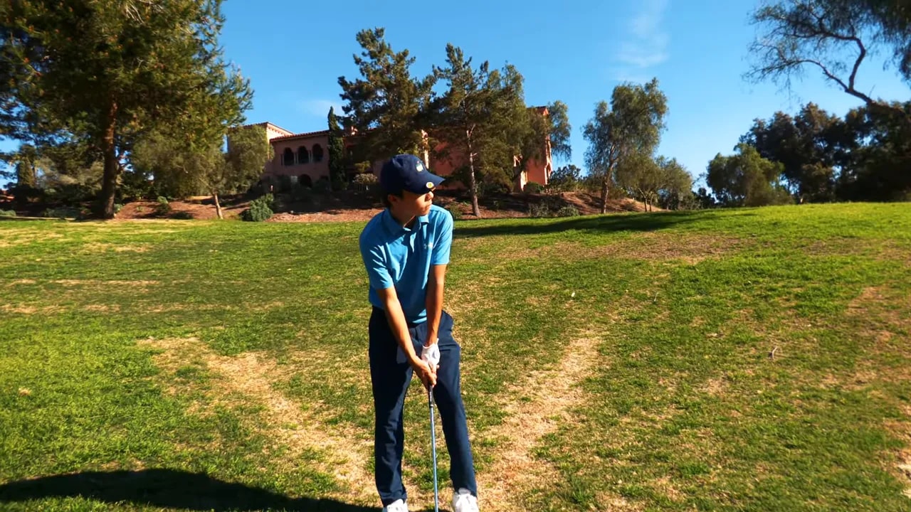 Golfer in address position on a slope preparing for an approach shot