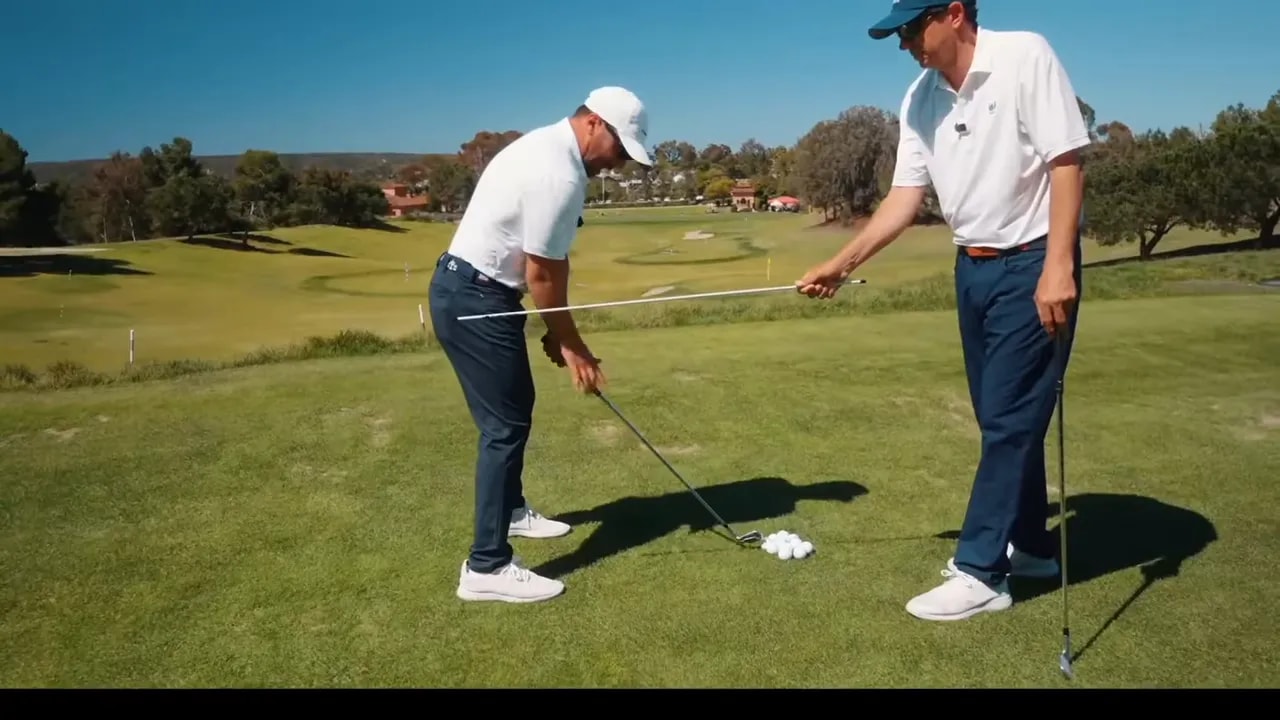 Instructor demonstrating golf takeaway hinge with alignment rod showing shaft in front of forearm at address