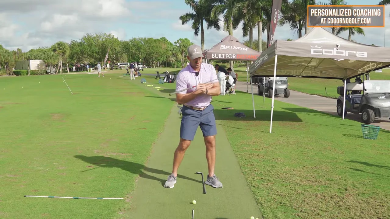 Golf coach at address position on a practice range using alignment cues for a two-club shoulder turn drill