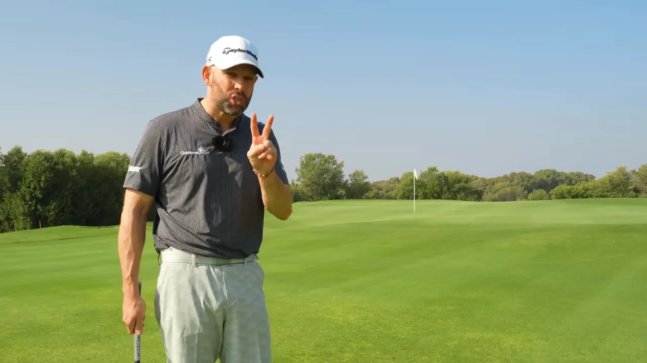 Golf instructor standing on the green holding up two fingers to illustrate two key steps for better pitching.