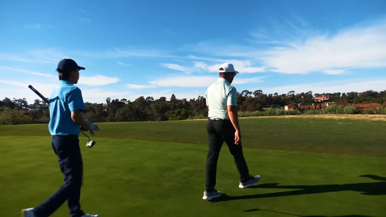 Two golfers walking off the green away from the camera with clubs, heading toward the next hole