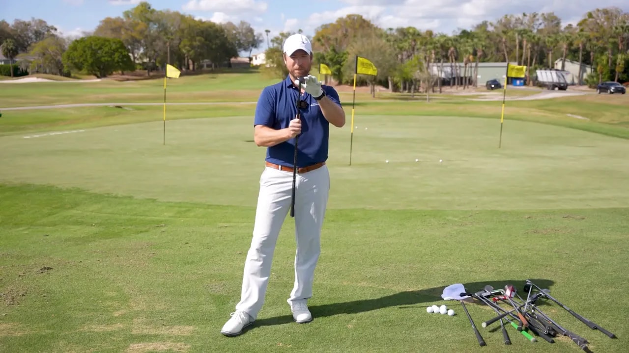 Golf instructor demonstrating a chipper address position with the club grounded on a practice green