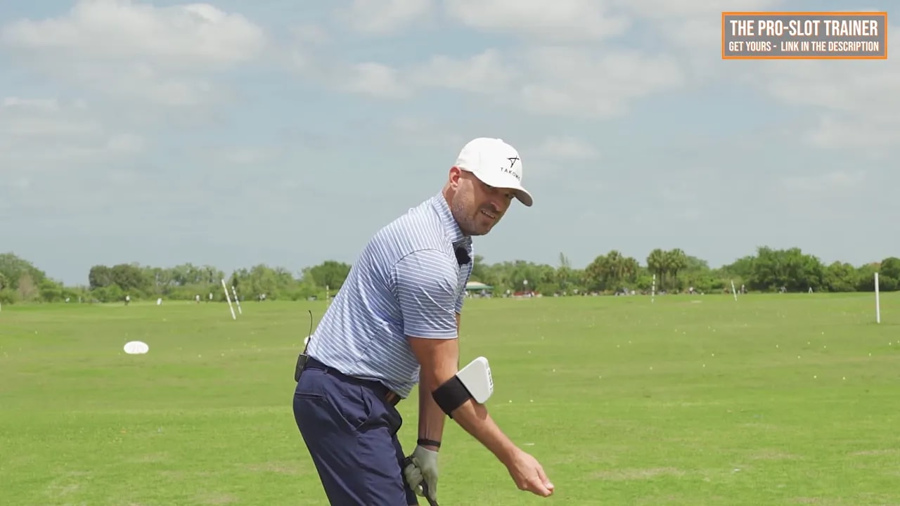 Coach demonstrating right elbow setup at address with bent, soft, under trail arm feel on a golf practice range