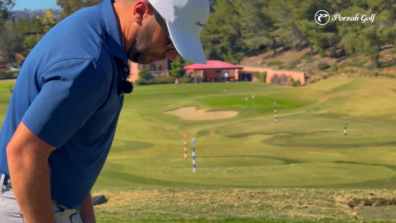 Coach demonstrating takeaway alignment on a practice range with boundary markers visible