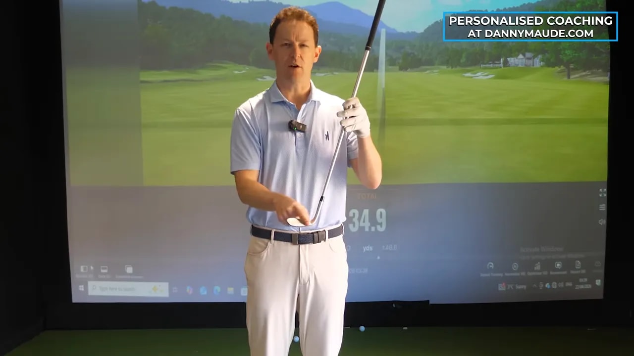 Golf coach holding a club up to demonstrate strike feedback and ball striking evidence in an indoor simulator