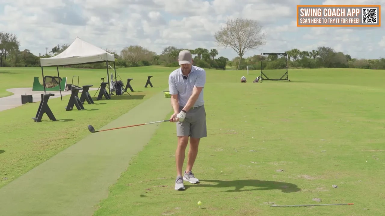 Golf coach addressing a ball on a practice range while demonstrating weak right driver shot troubleshooting